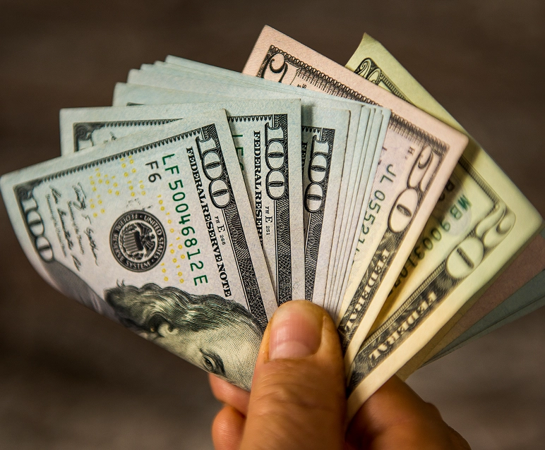 Hand holding multiple US dollar bills.